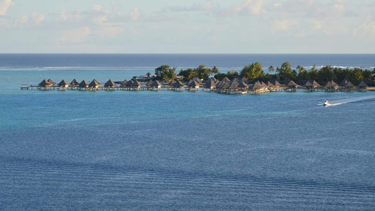 Taha'a / Society Islands overwater bungalow resort on turquoise lagoon, day, pale blue sky