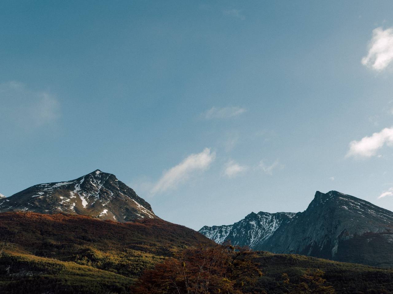 Snow-dusted Fuegian Andes peaks near Ushuaia under pale blue sky with autumn forest slopes