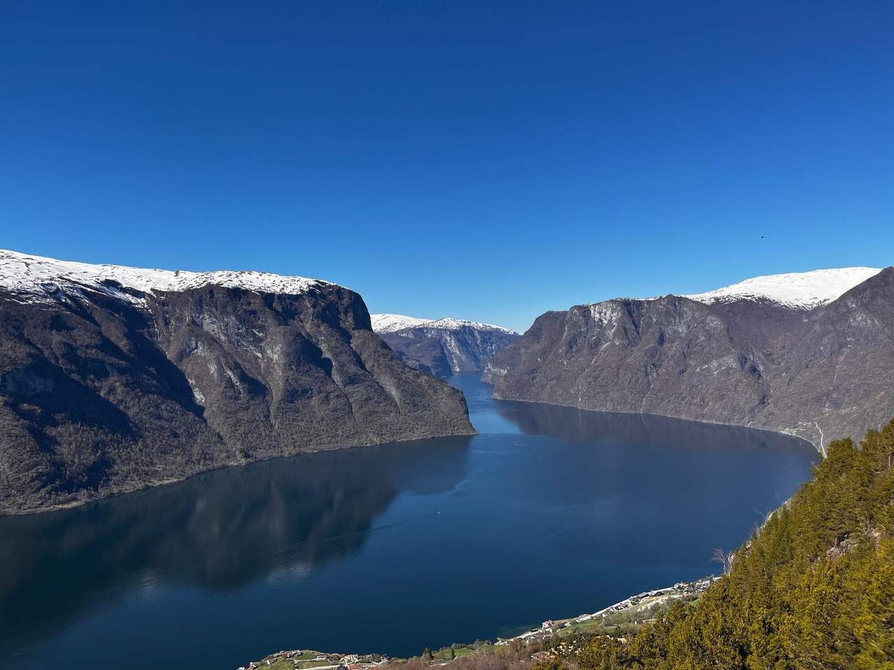 Aerial Sognefjord with snow-capped peaks and shoreline villages under clear blue sky (Vikøyri / Sognefjord character), day