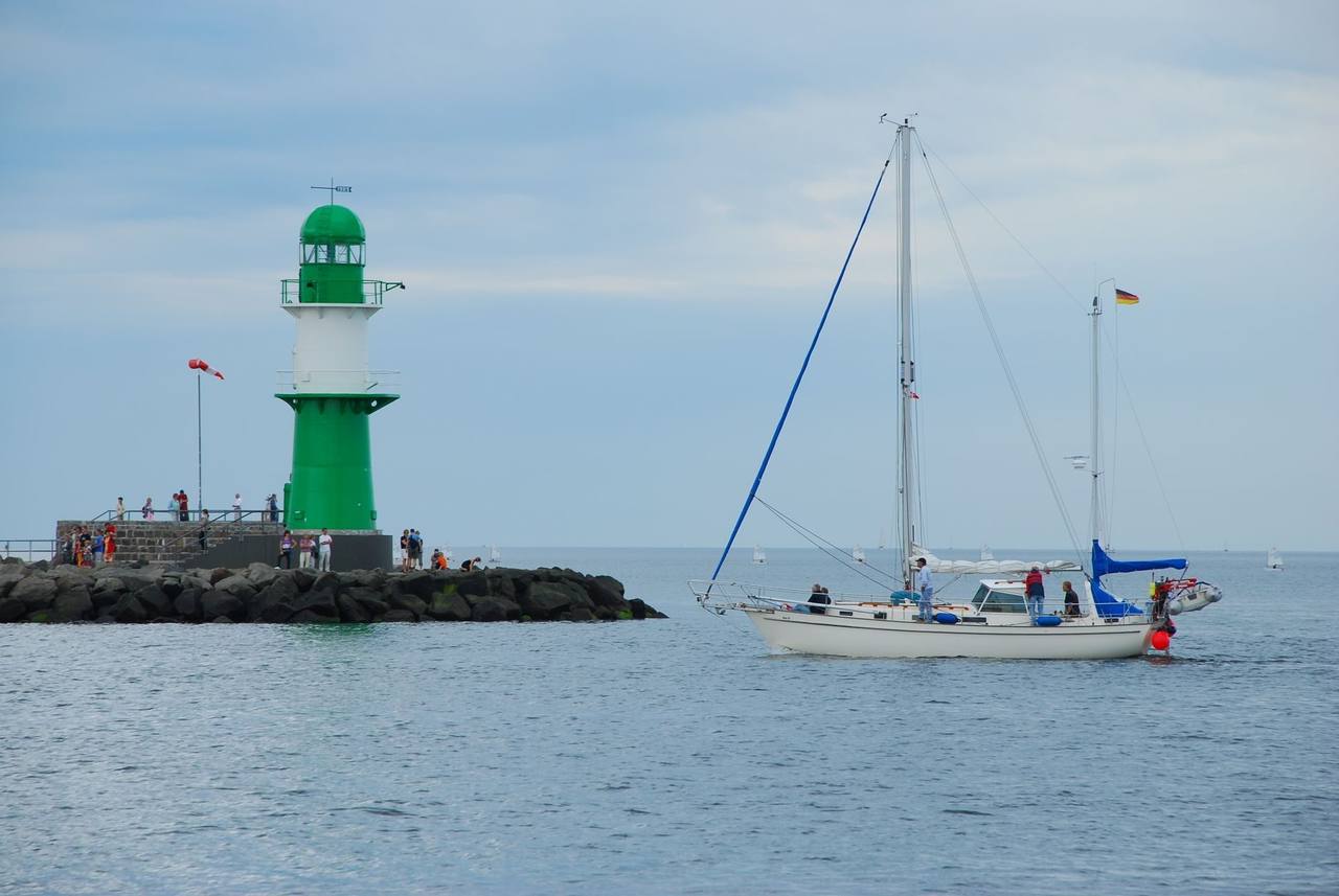 Warnemünde green-and-white lighthouse on the mole with sailboat, day, blue sky