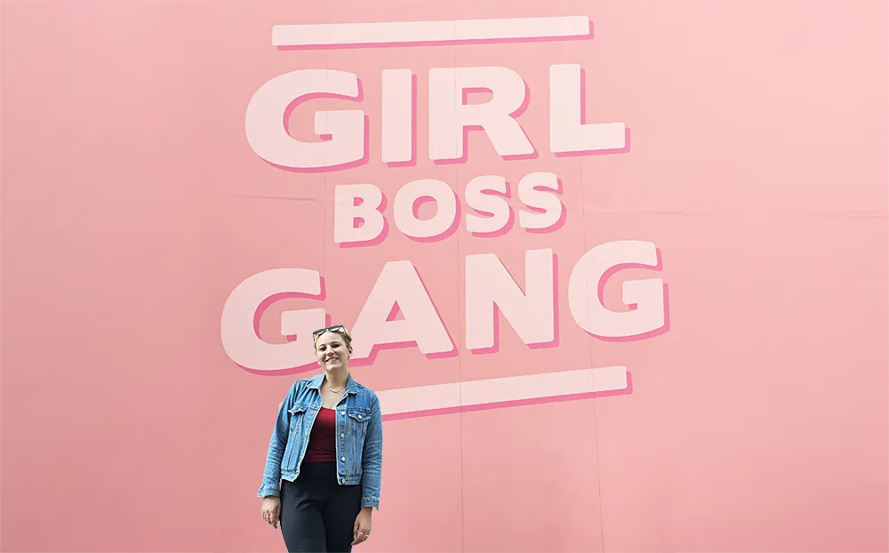 Emma in front of a wall with a graphic that reads "Girl Boss Gang"