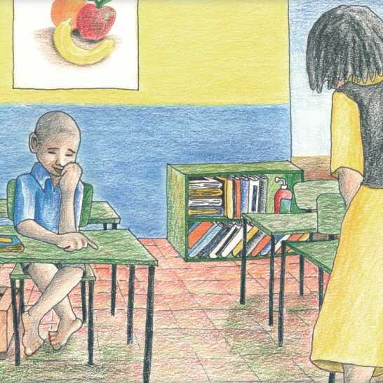 A sad-looking boy sitting at a desk in a classroom and a teacher standing in front of him. 