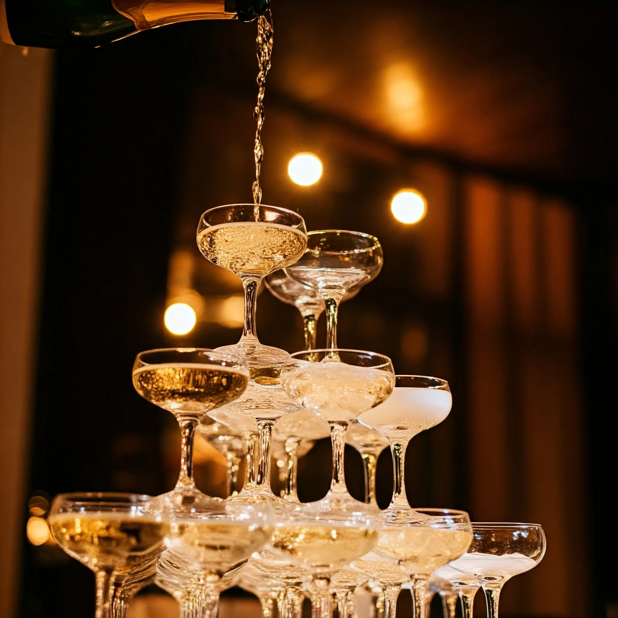 A tower of champagne glasses where the champagne is poured, each glass softly glowing as it fills.