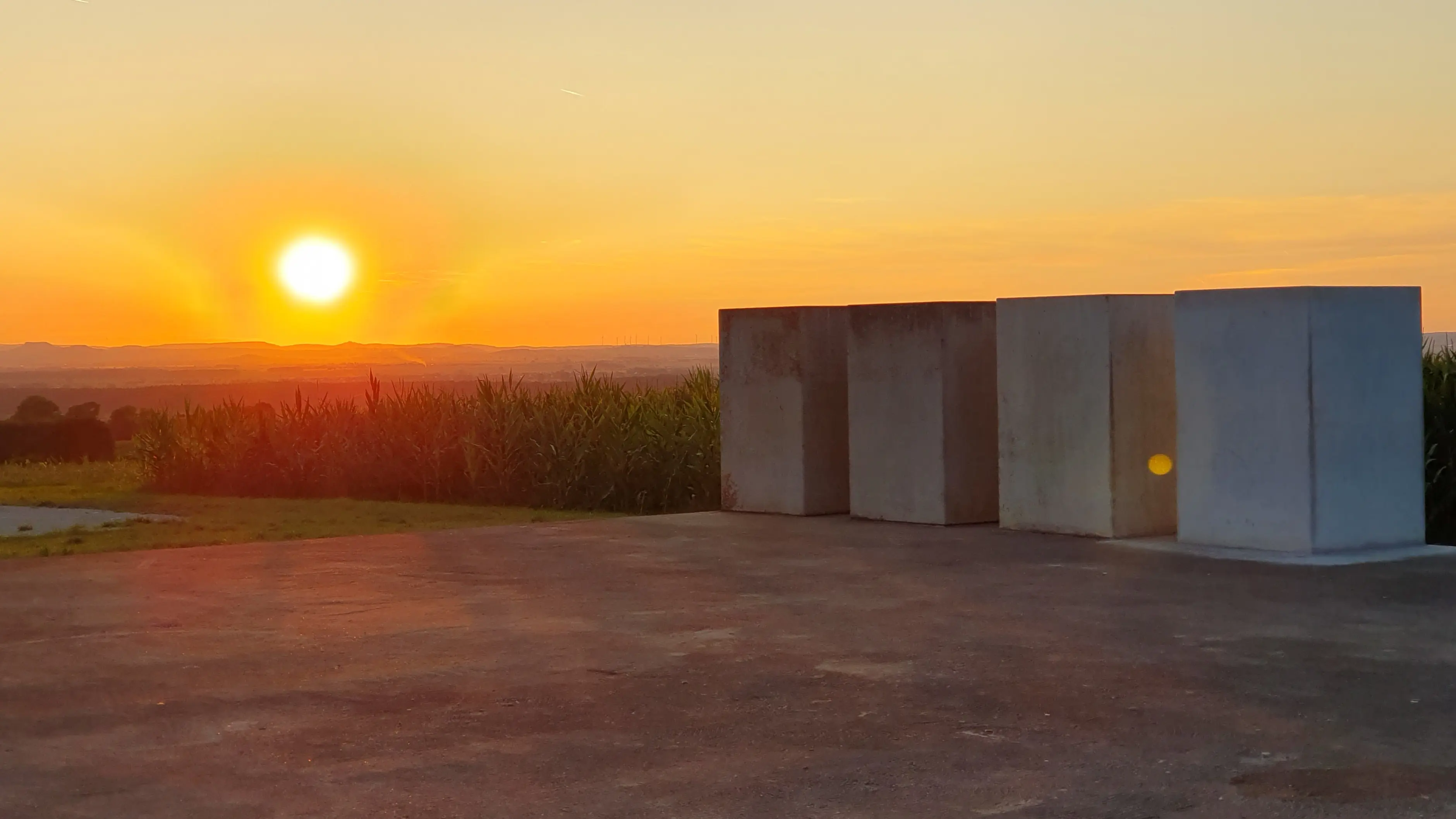 Sunset over an open paved area, with a row of concrete blocks on the right and golden light across the horizon