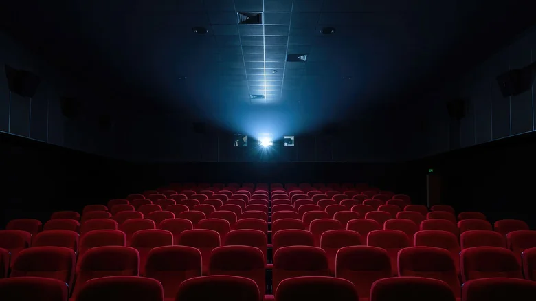 Empty cinema with row upon row of empty red seats, with the bright glare of the projector in the back.