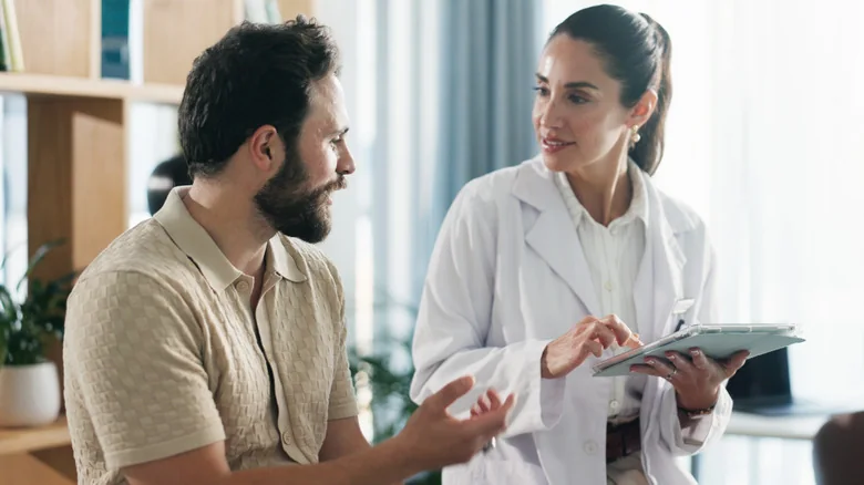 Doctor speaking to a man while holding a tablet.
