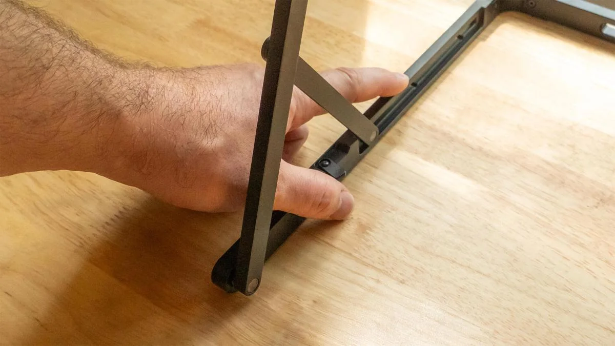 A hand demonstrates the Aura Triple 15.6" Aero Pro Max's stand design concerns.