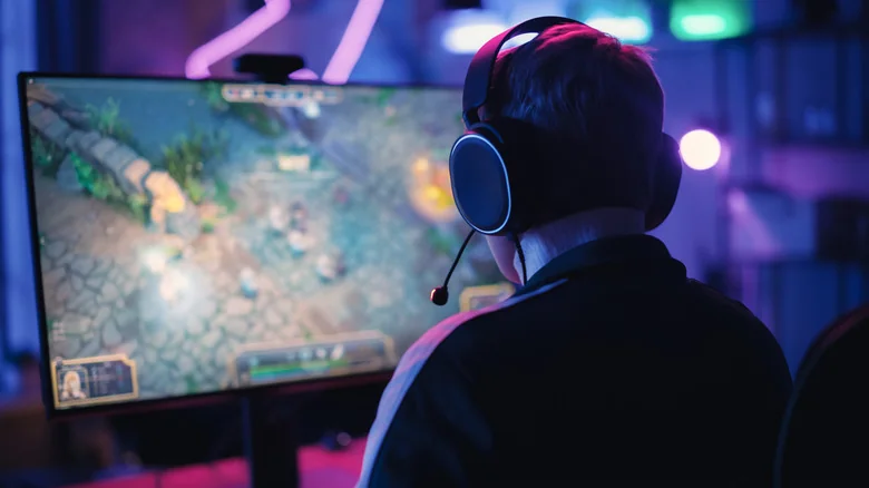 Person wearing a headset playing PC games in a dark room in front of a computer monitor.