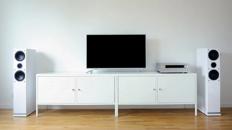 White entertainment center with a TV on top, directly centered, flanked by two tall, white speakers.