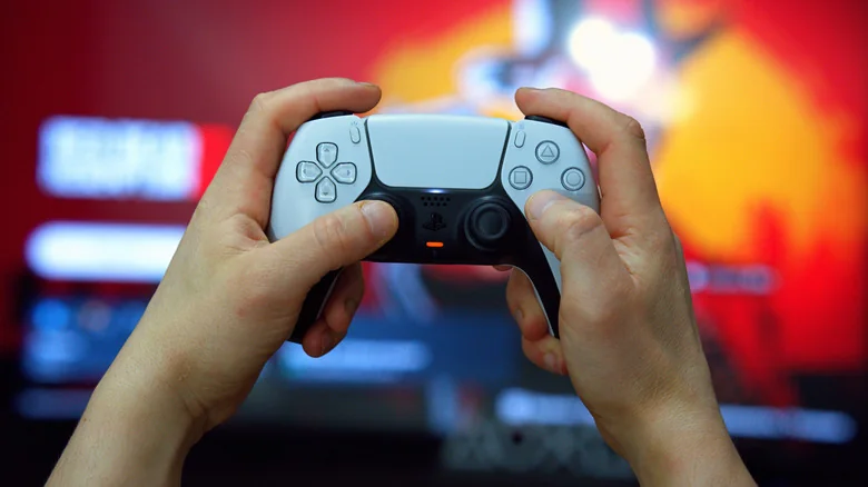 A person holding up a white Sony PlayStation DualSense controller.