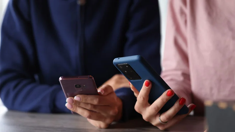 The hands of two people holding phones at a table.