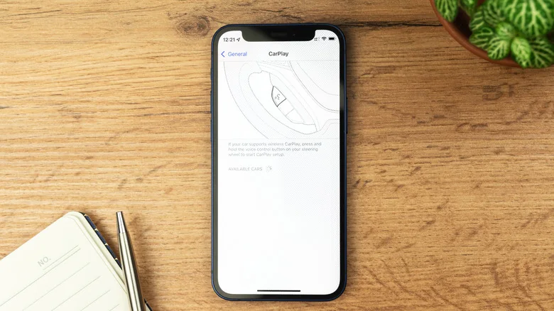The CarPlay menu on an iPhone, on a table with a notebook and plant nearby.