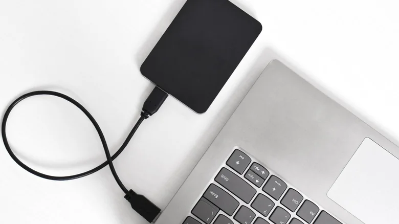 A black external hard drive plugged in to a silver laptop.