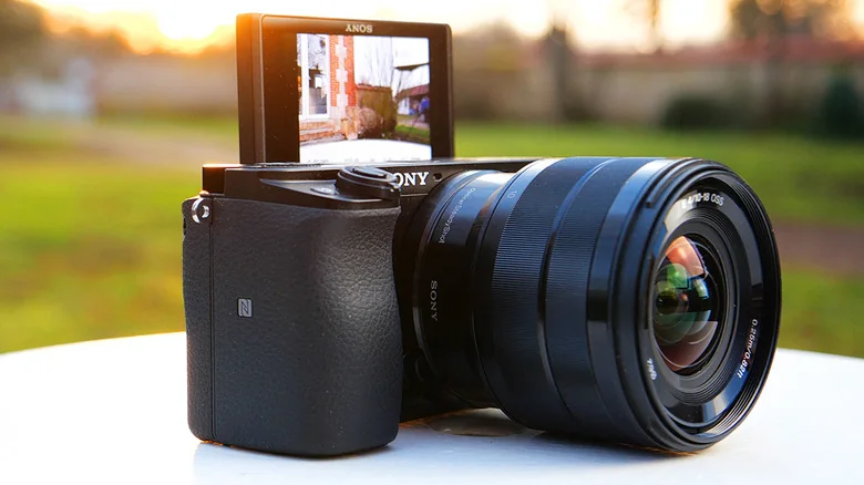 Sony A6100 mirrorless camera is shown at sunset with the rear display flipped up.