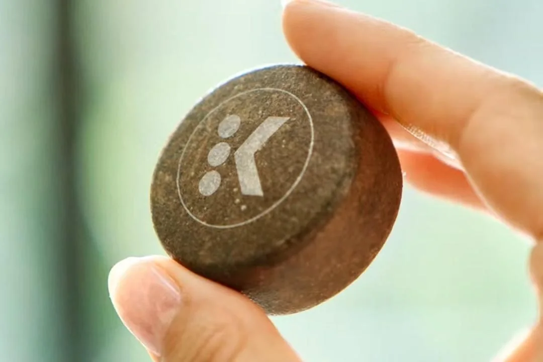 A person holds a single Keurig AltaRounds in their fingers.