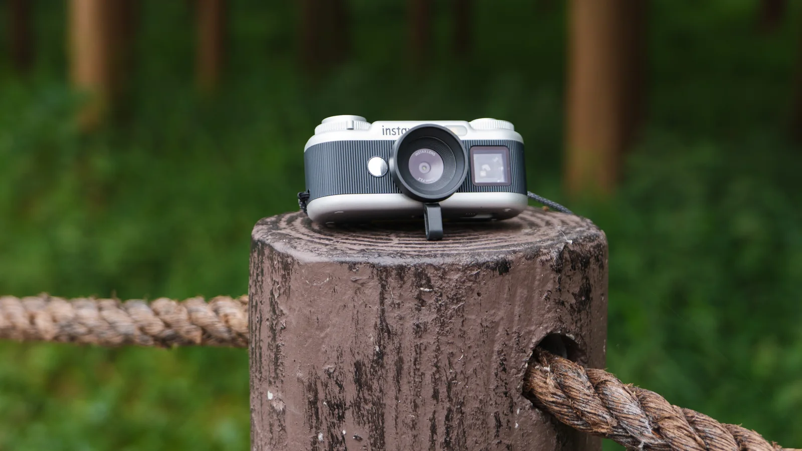 Fujifilm Instax Pal 2 digital camera on a wooden post next to a forest, it's propped up with its selfie aide
