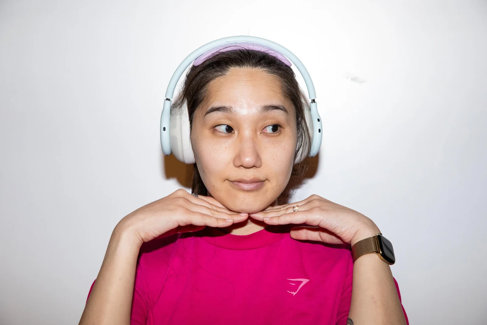 A woman wearing white Beats 360 headphones with her hands up under her chin.