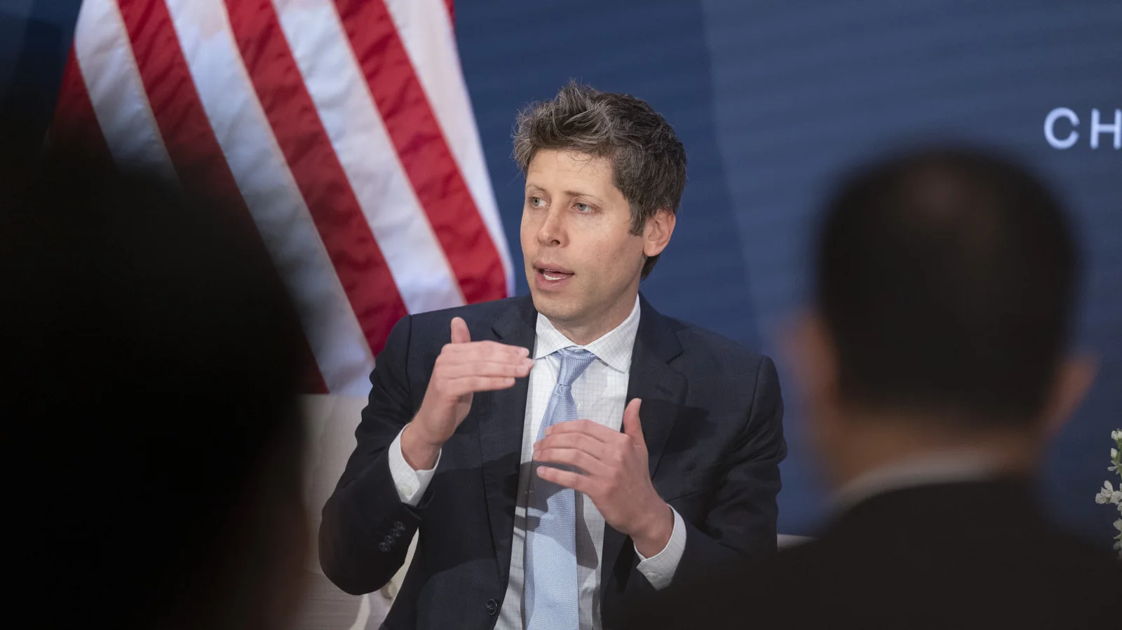 A man in a suit with the US flag in the background.