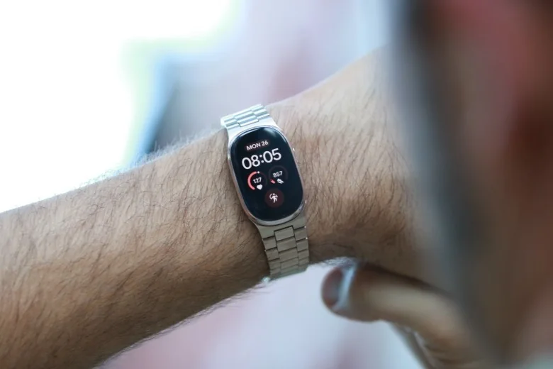 A Fitbit Edge with gold Metal Links band on a wrist held in mid air.