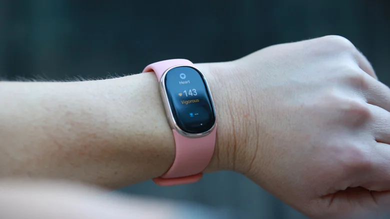 A Fitbit Edge on the wrist of a person showing the heart app on its screen. The heart rate reading says 143.