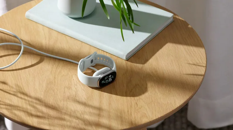 A Fitbit Edge charging on a side table.