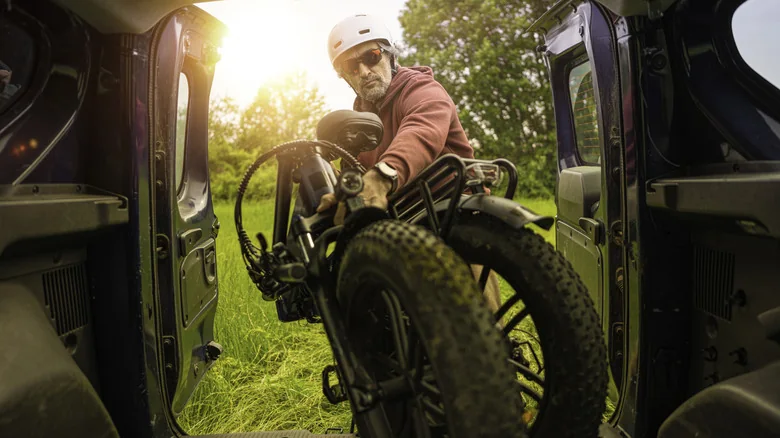 A person unloading his folded e-bike from the back of a vehicle.