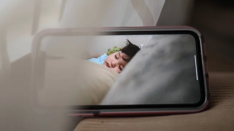 A smartphone displaying a sleeping baby in a cozy, indoor setting, conveying warmth and care.