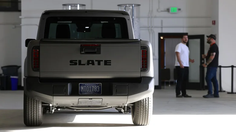 A tan Slate truck parked in a garage and viewed from behind, with two people standing in the background.
