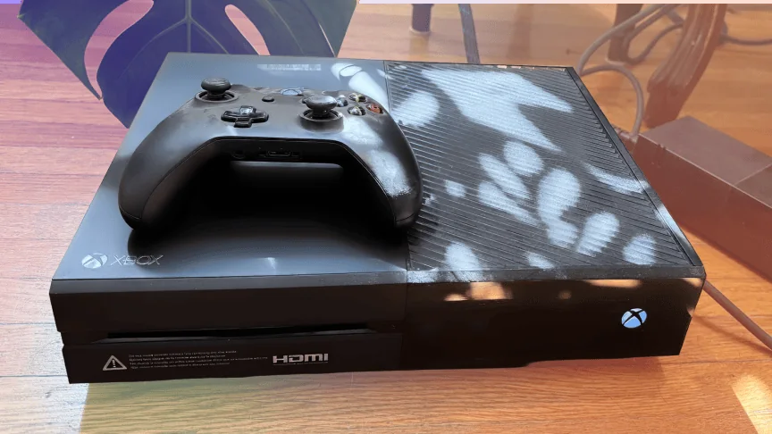 An Xbox One with a controller on top of it.