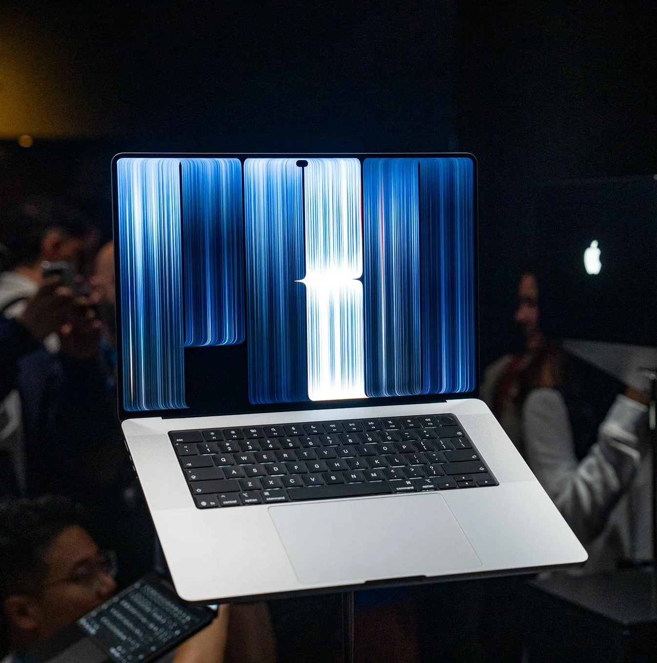 The MacBook Pro with PROLED XDR display on a pedestal in crowded press area.