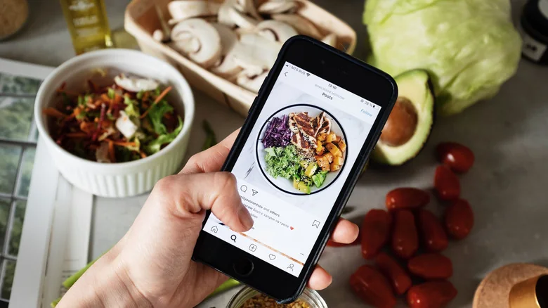 Person making a healthy salad using ingredients on the phone screen.