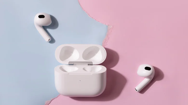 AirPods outside of their charging case on a blue and pink background.