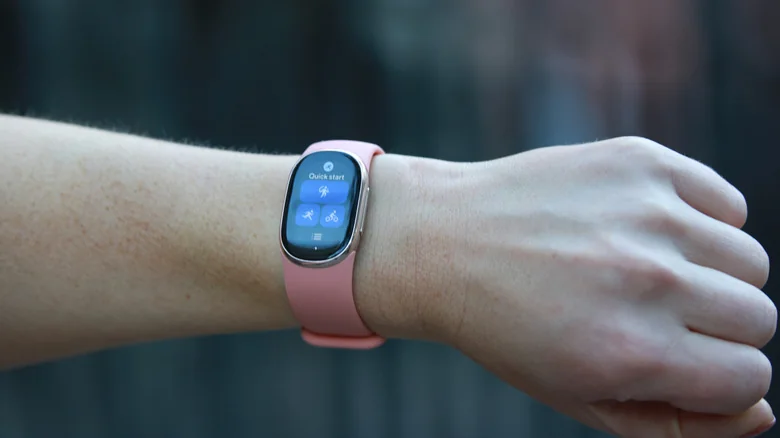 A Fitbit Edge with a pink band on a person's wrist, showing the Quick Start tile.