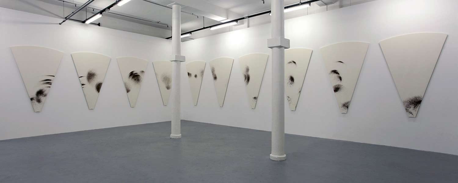 Image of a brightly-lit gallery, ten pie-slice-shaped canvases on the wall with random-looking marks on them