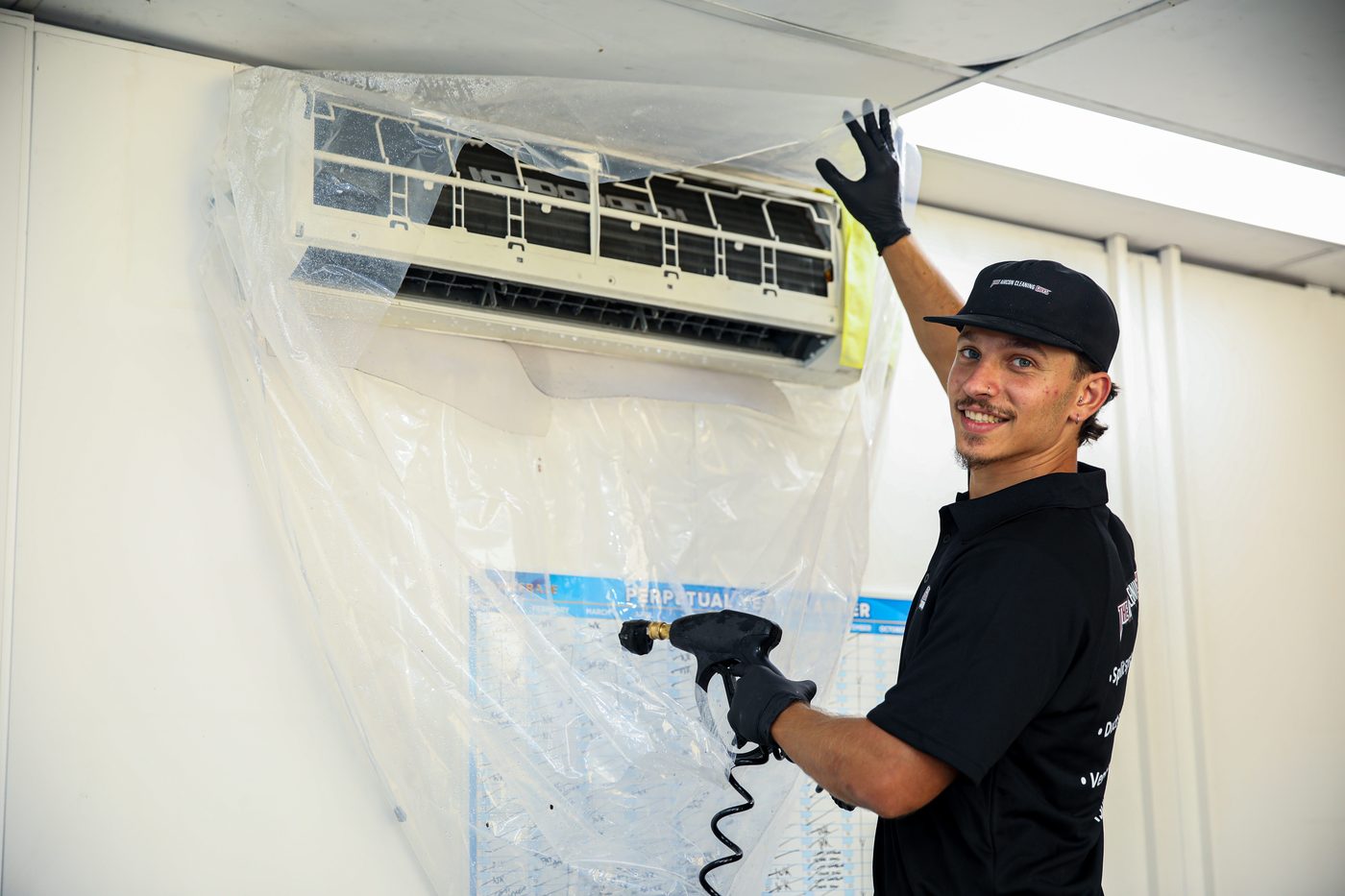 Aircon cleaning technician with containment bag fitted to split system unit ready for deep clean Sydney