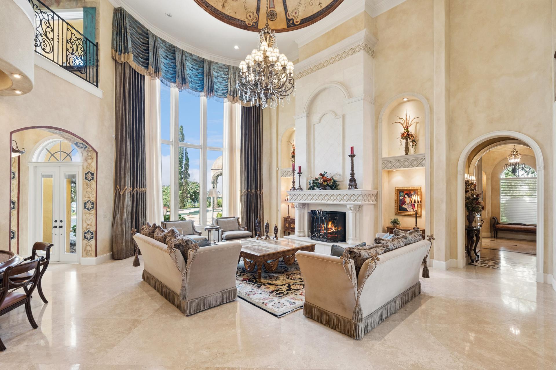 The living room at 2961 Lakeview Dr, with 30-foot floor-to-ceiling windows, a grand limestone fireplace and a hand-painted domed ceiling