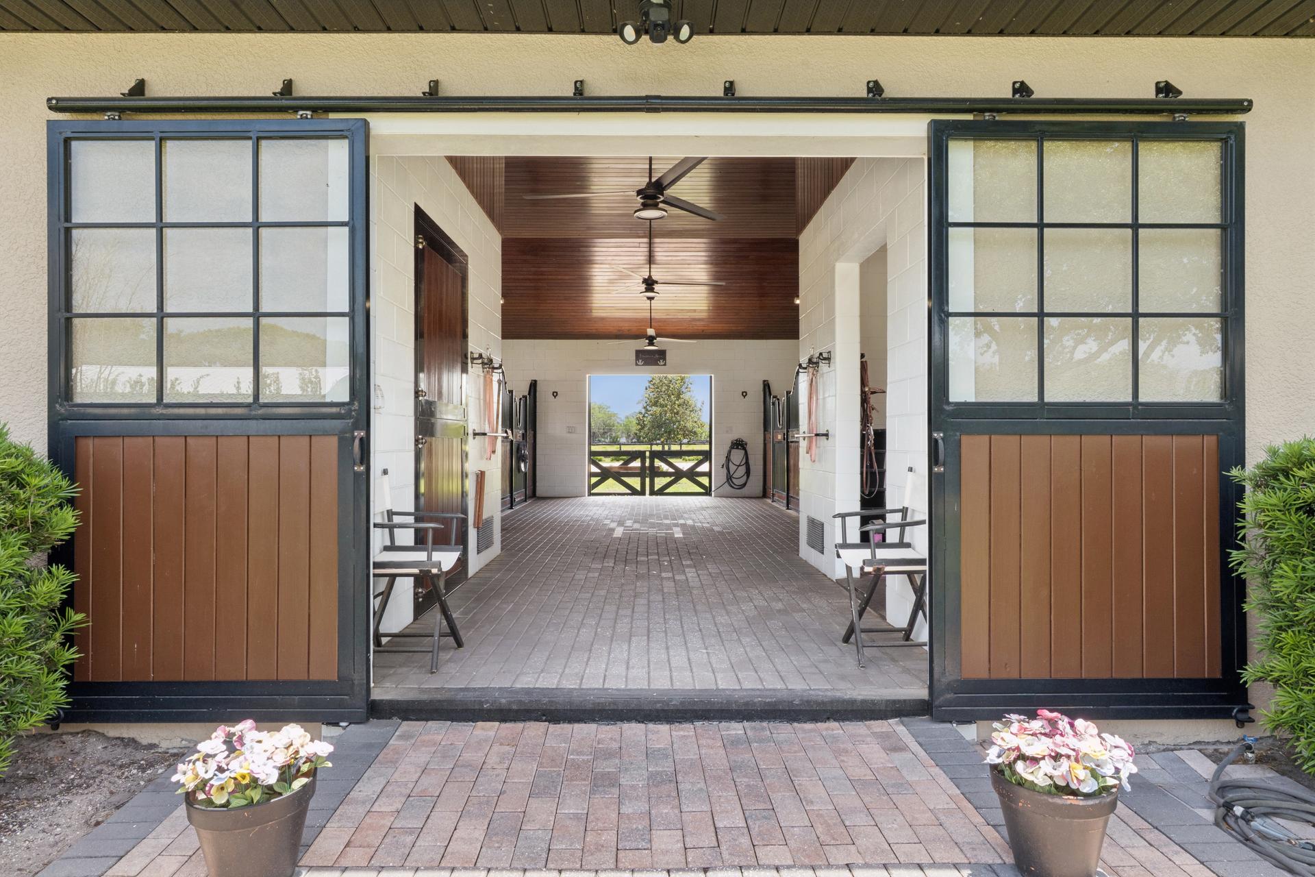 The barn breezeway at 746/0 Lake Mills Road — sliding barn doors standing open at the end of a brick-paved aisle, looking through to the paddocks beyond
