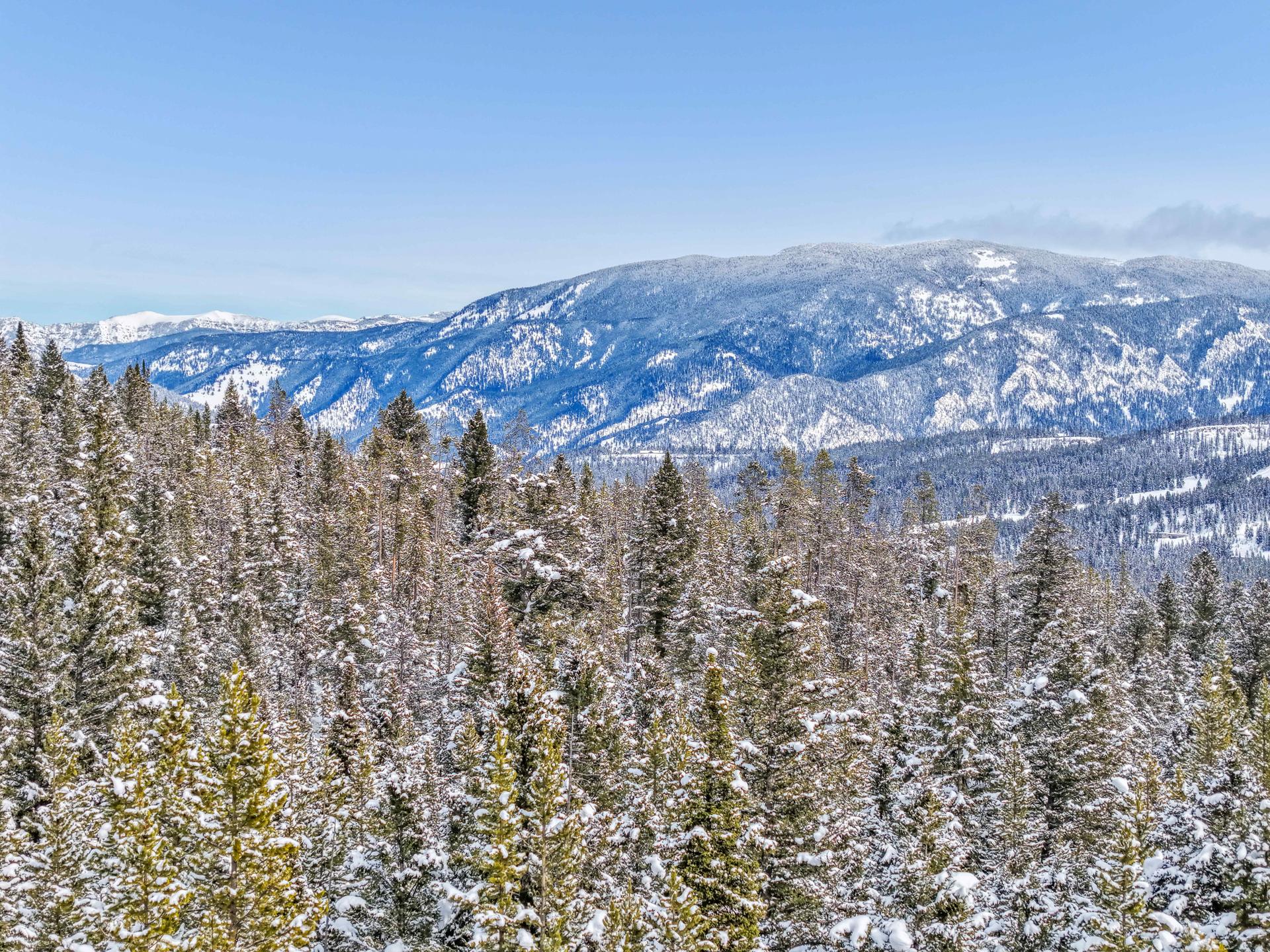 Long mountain views east from the Lot 88 Crown Butte homesite over snow-covered forest toward the Gallatin Mountain Range