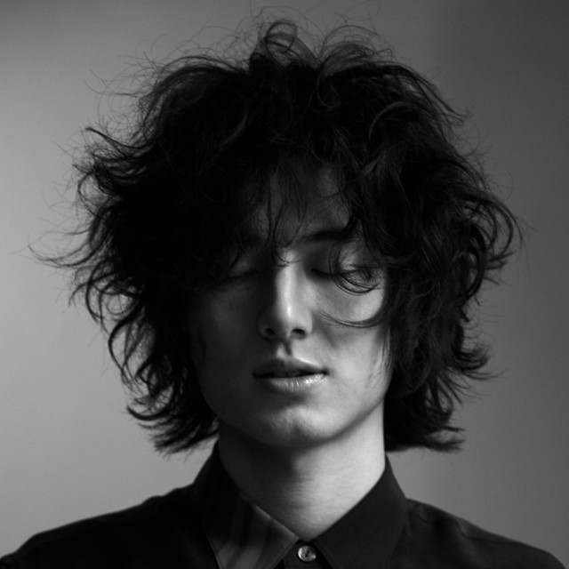 Black and white photo of Fujii Kaze with his eyes closed, his long hair styled to be unkempt