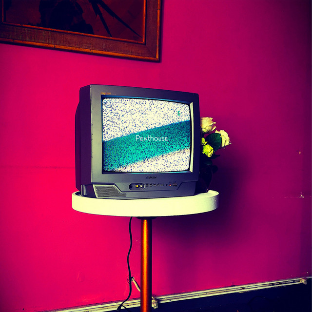 A CRT TV switched on but with no image placed on a table against a bright pink wall