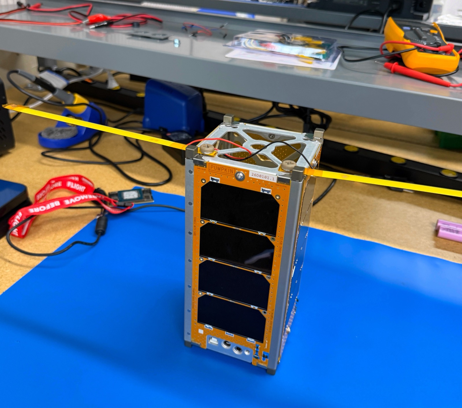 작동대 위에 조립된 KENSAT 2U flatsat 사진으로 펌킨 섀시, 보디-장착 태양전지패널, 전선 및 Remove-Before-Flight 태그가 보여진다.