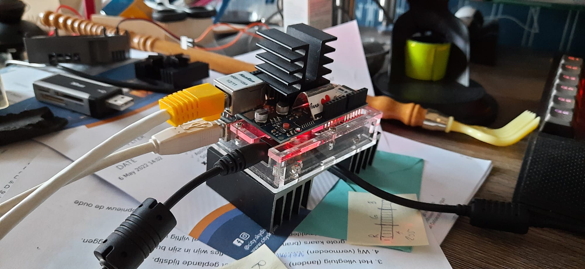 An Arduino with an Ethernet shield on it, standing on a large cooling block to cool the Arduino. And a medium cooling block balancing on a small cooling block sitting on the Ethernet shield's cpu being kept in place by 2 pieces of cardboard cut from a candy box.