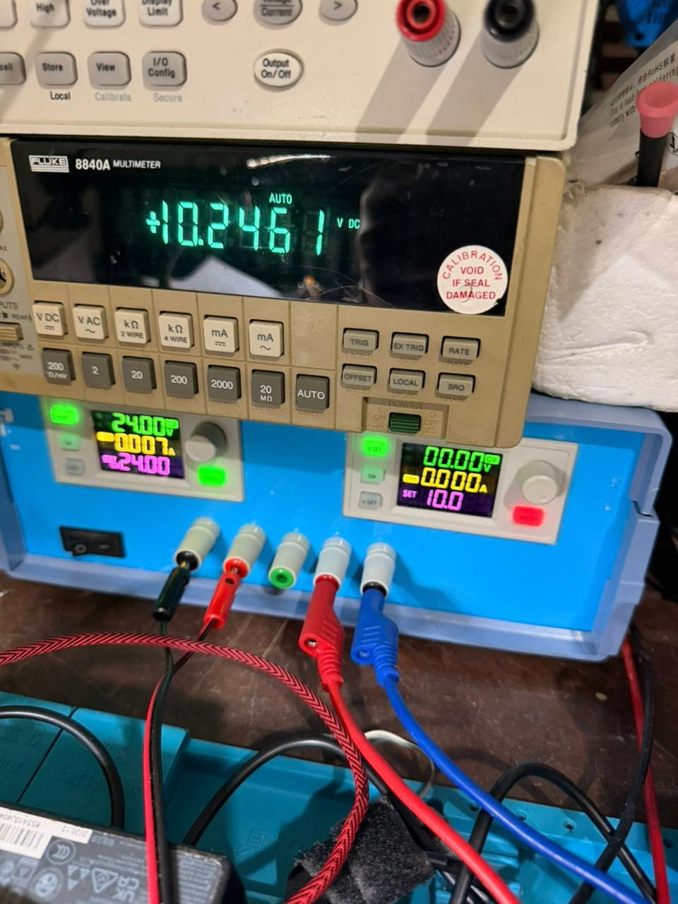 Dual SK120X supply in blue enclosure stacked under a Fluke 8840A; binding posts and live readouts