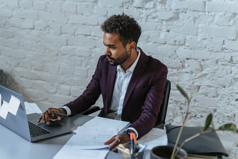 Professional man with curly hair working on a laptop in a stylish office setting.
