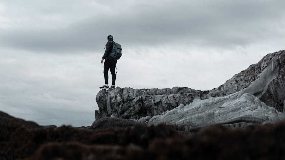 A lone hiker stands at the edge of a rugged cliff with a moody sky overhead, epitomizing adventure.
