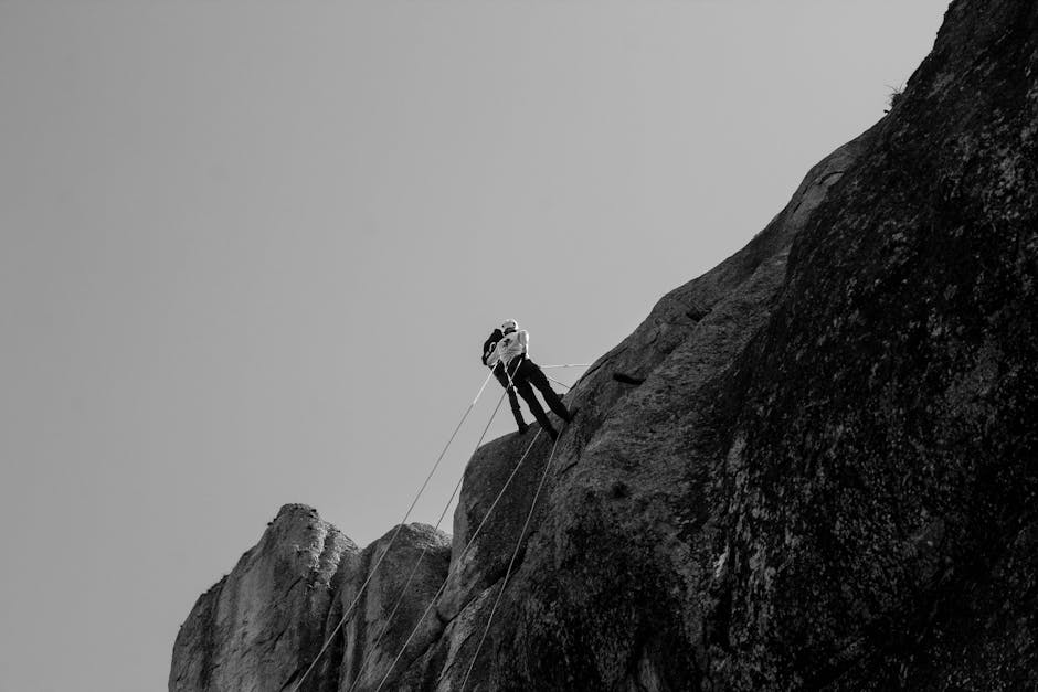 Black and white image of a climber conquering a steep cliff, showcasing strength and determination.