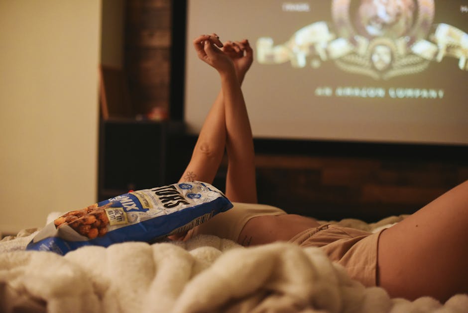 Relaxing movie night at home, lying in bed with snacks and a projector.