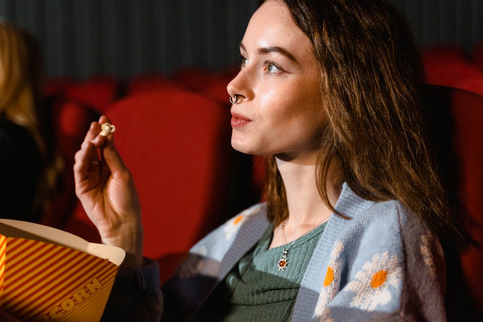 A young woman enjoys popcorn while watching a movie in a cinema theater.