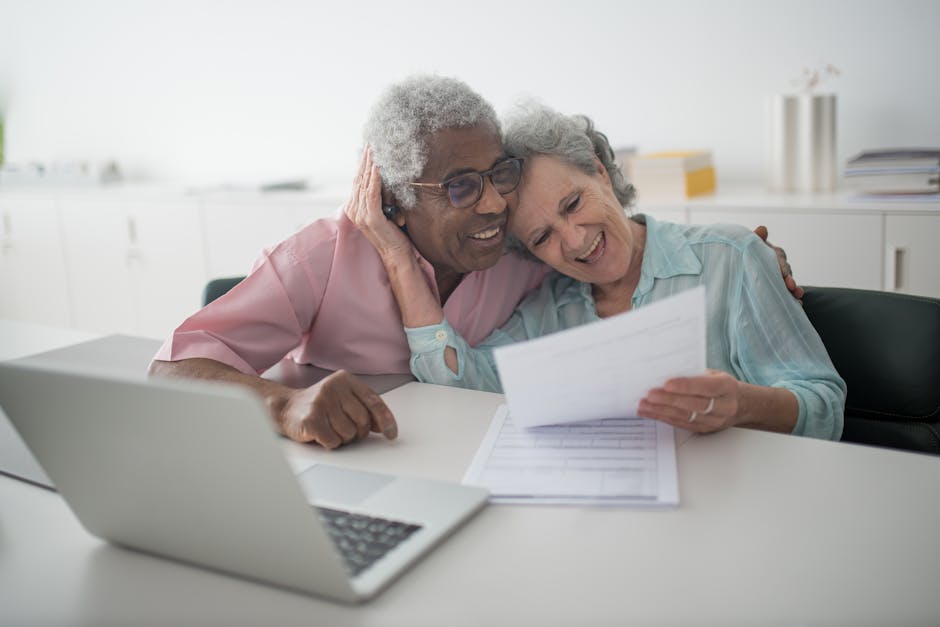A joyful senior couple smiling while reviewing documents together at a desk with a laptop.