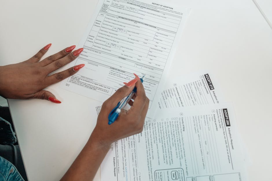 A woman with red nails fills out adoption application forms on a desk.